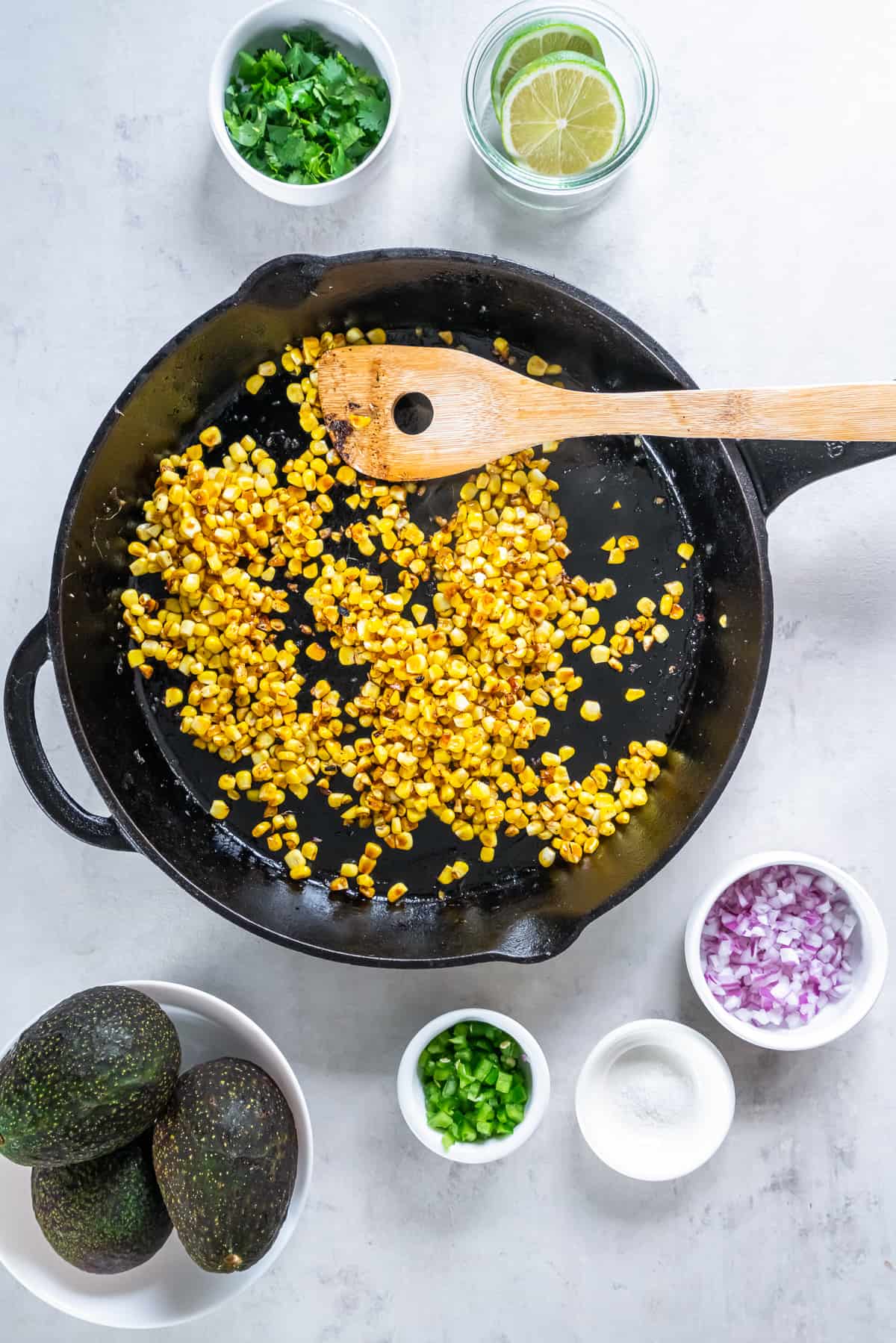 Corn in a cast iron skillet with ingredients surrounding it.