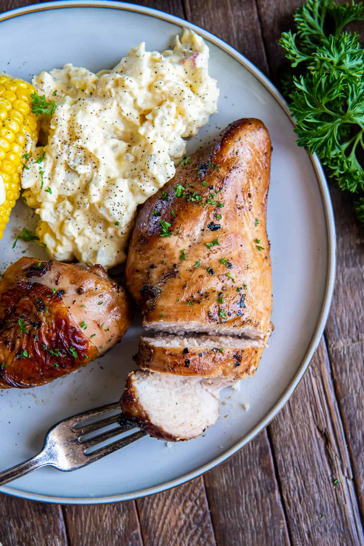 A top down shot of sliced grilled chicken breast on a plate being pierced by a fork.