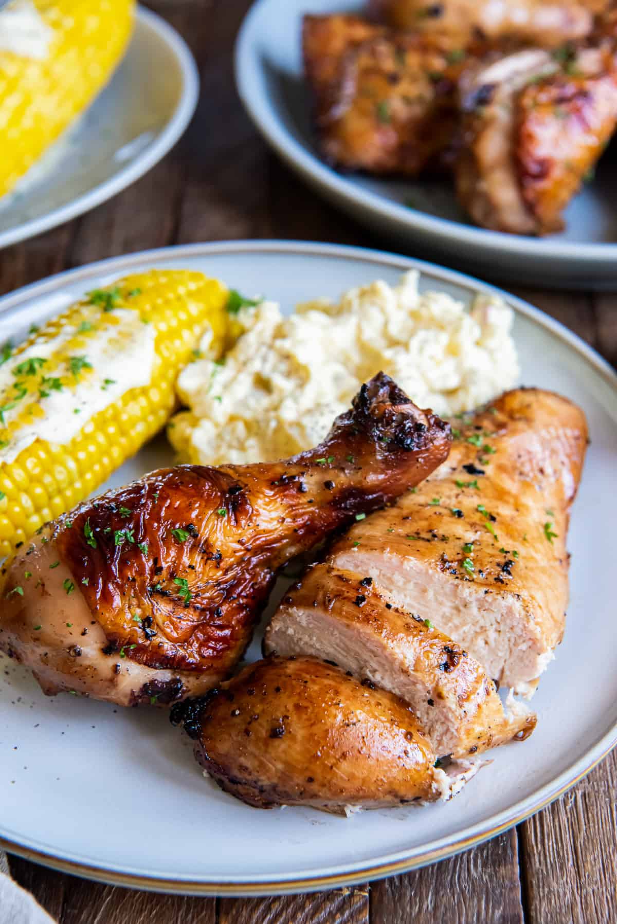 Sliced grilled chicken breast and a drumstick on a plate with corn and potatoes.