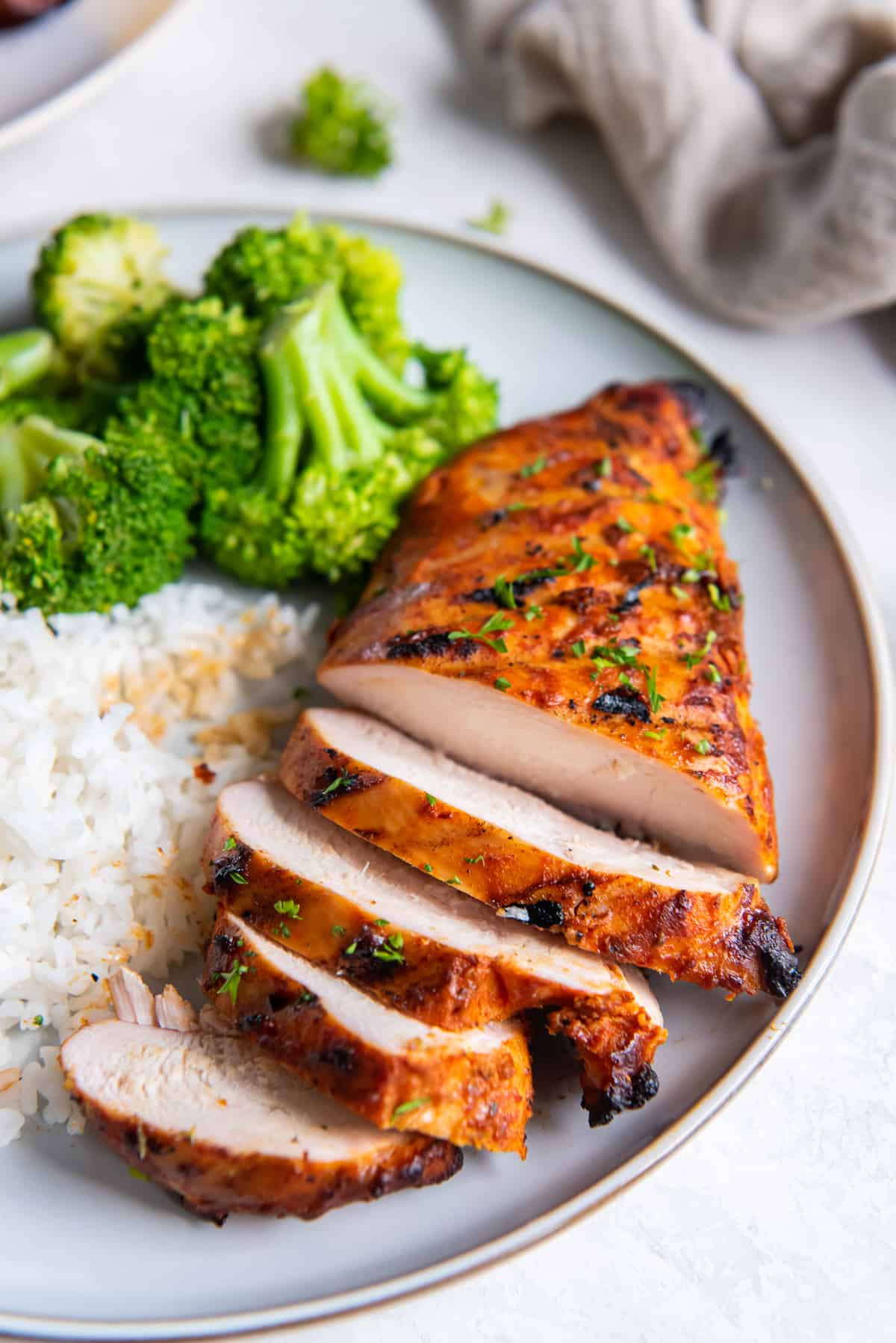 A sliced grilled chicken breast on a white plate with rice and broccoli.