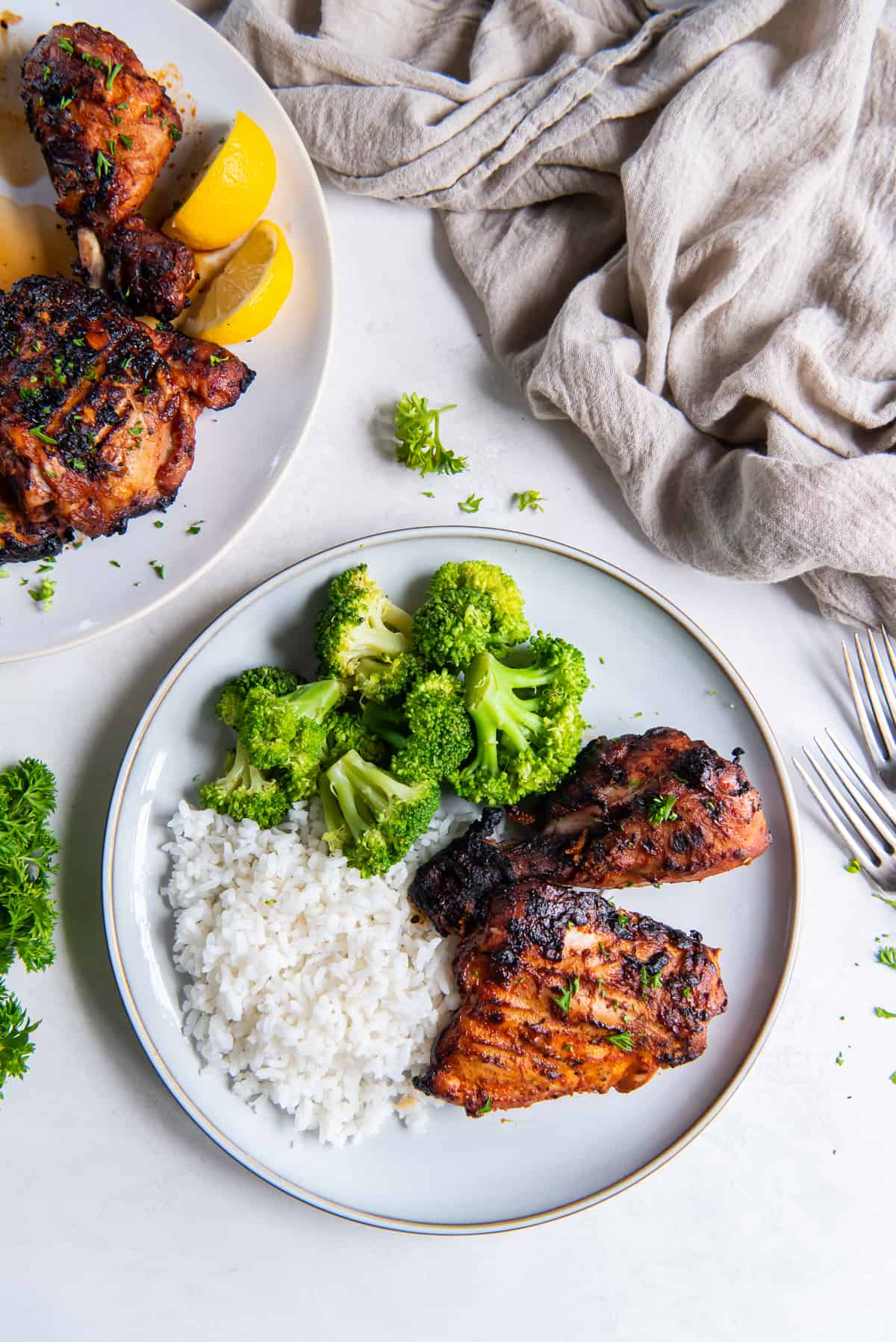 A top down shot of richly colored grilled paprika chicken on a white plate with rice and broccoli.