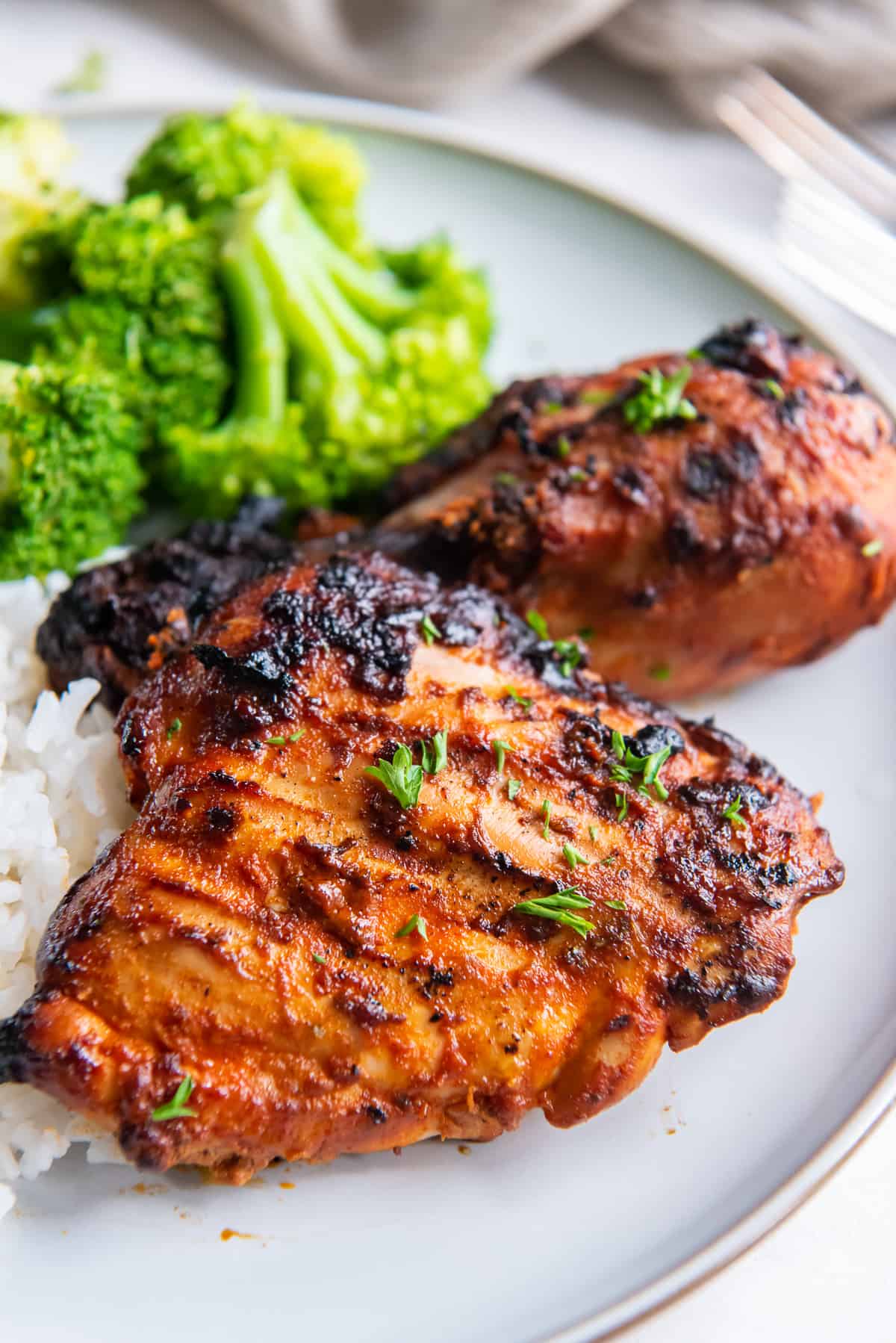 Grilled paprika chicken on a white plate with rice and broccoli.