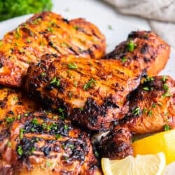 Richly colored paprika grilled chicken on a platter with lemon wedges.