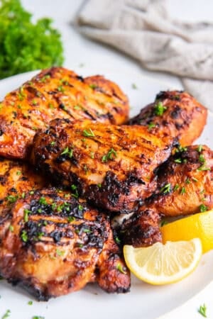 Richly colored paprika grilled chicken on a platter with lemon wedges.