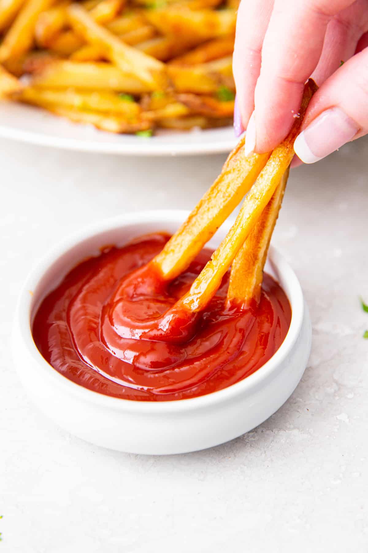 Fingers dipping 3 baked fries in ketchup.