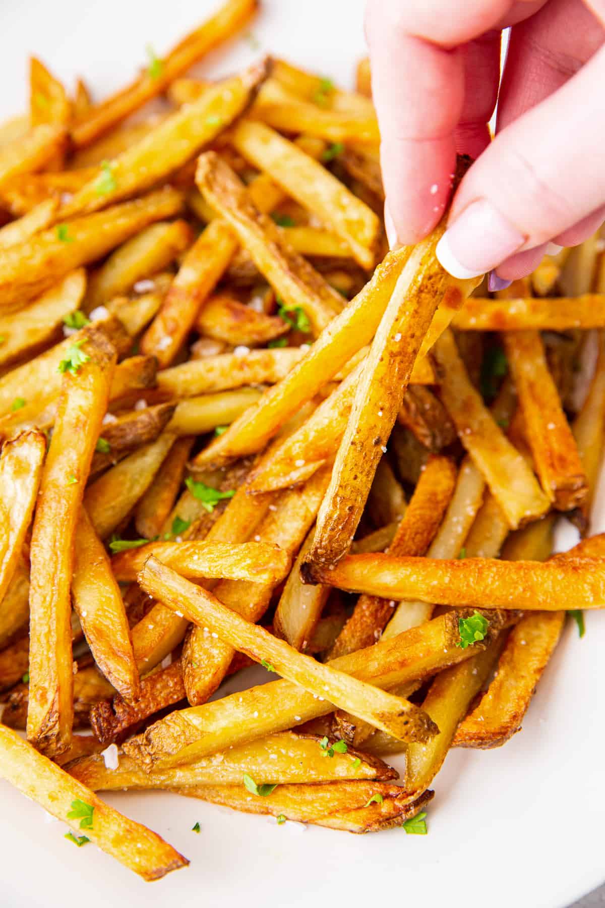 Fingers lifting french fries from a bowl.