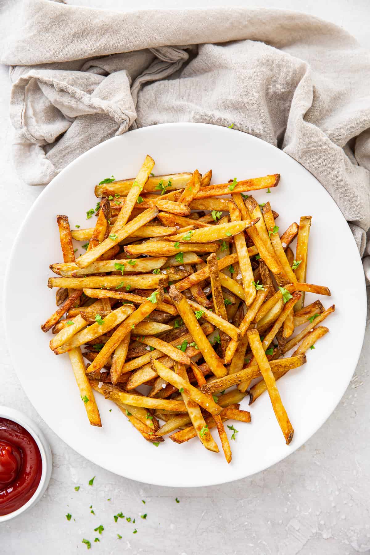 French fries and ketchup in white bowls near a grey cloth.