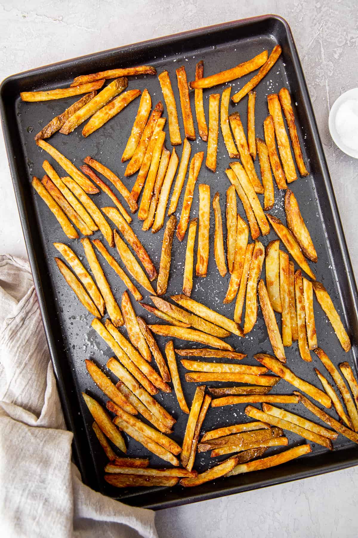 French fries on a rimmed baking sheet after baking in the oven.