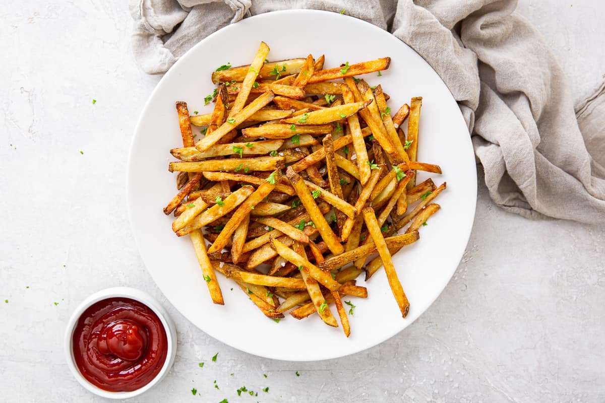 French fries and ketchup in white bowls near a grey cloth.