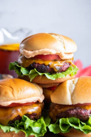 Three burgers on brioche buns stacked on a platter.