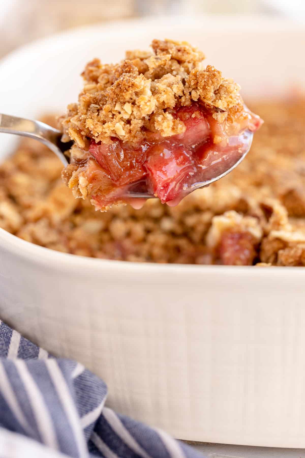 A spoon scooping Rhubarb Crisp from a white baking dish.