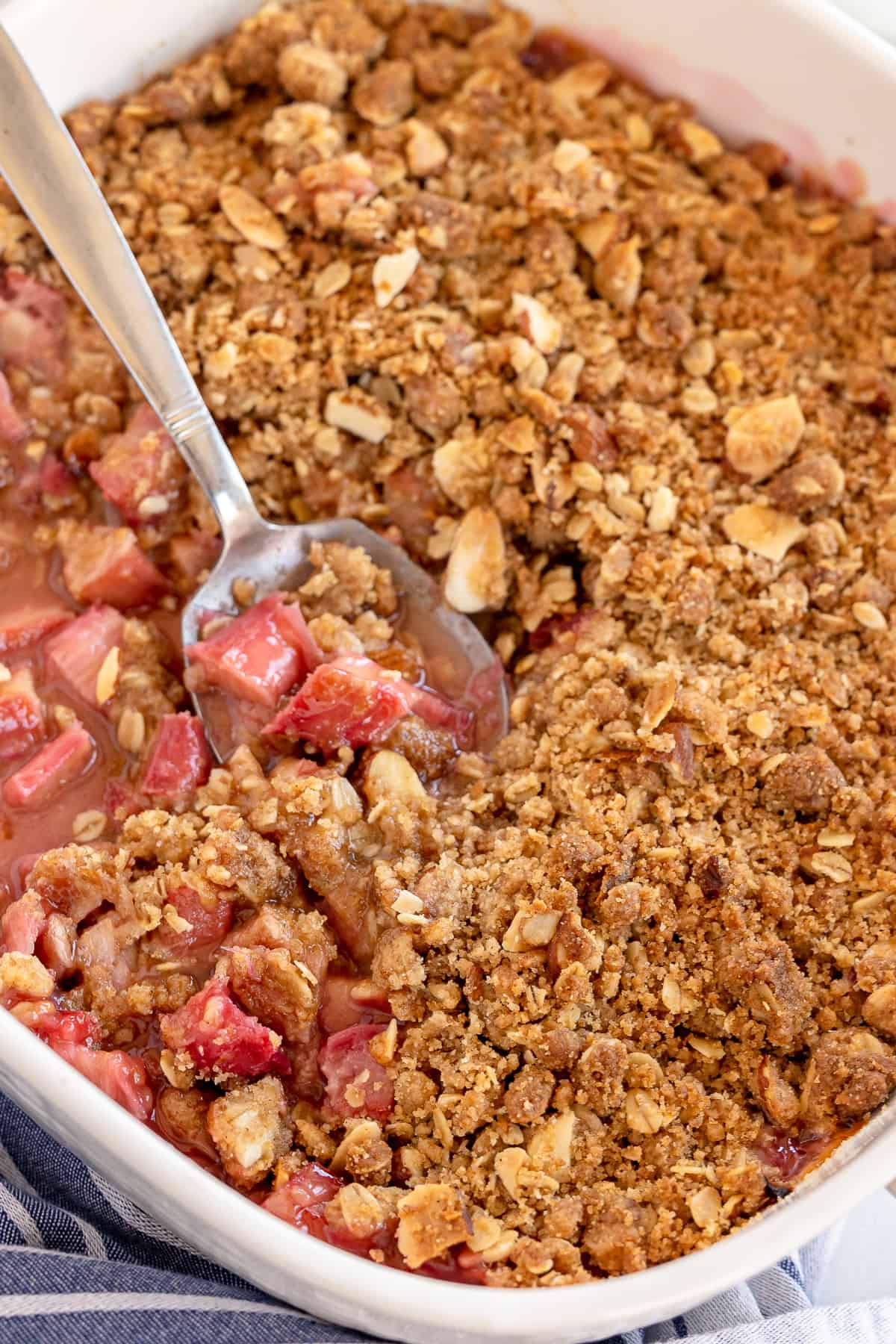 A spoon scoops Rhubarb Crisp from a baking dish.