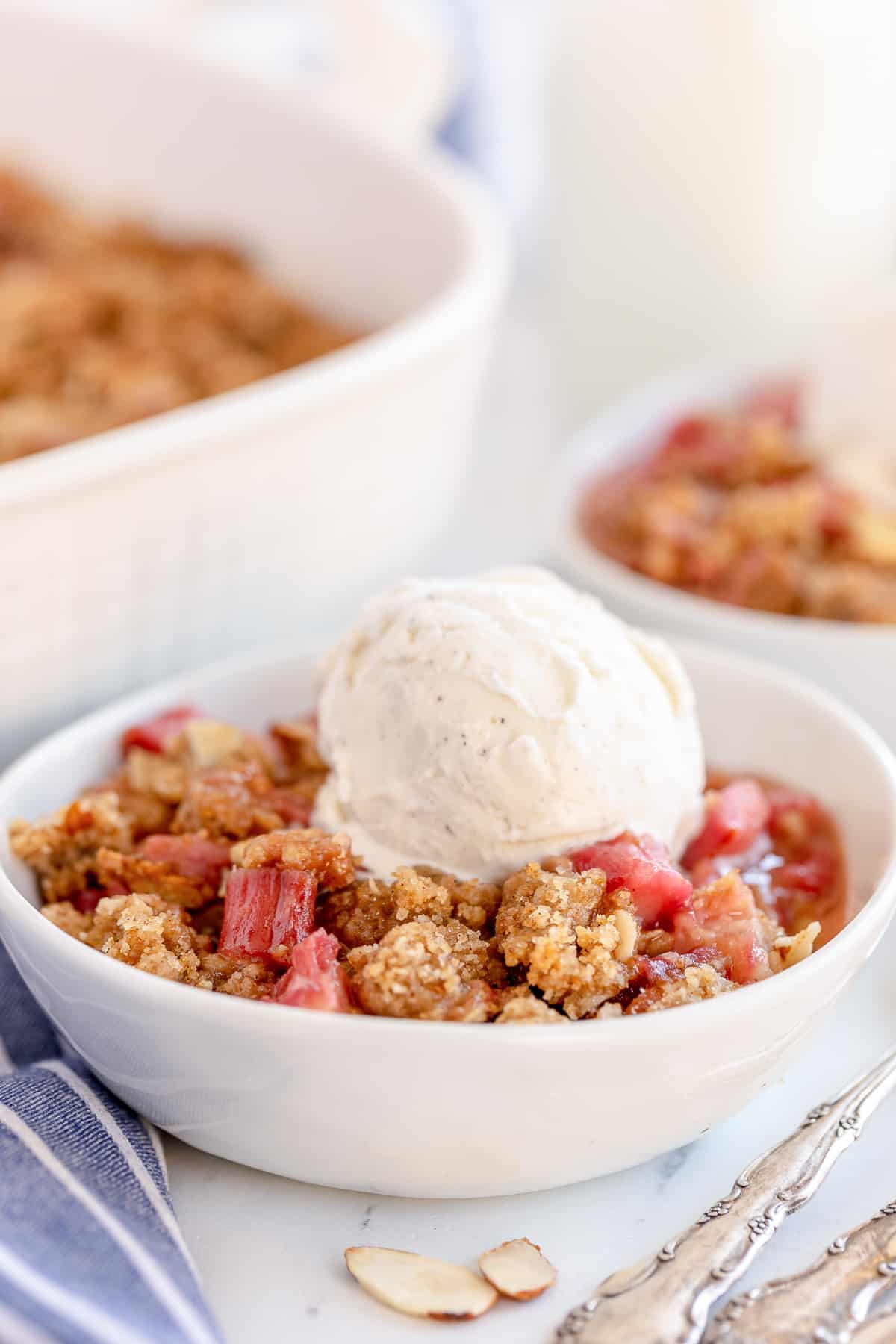 Rhubarb crisp in a white bowl topped with vanilla ice cream.