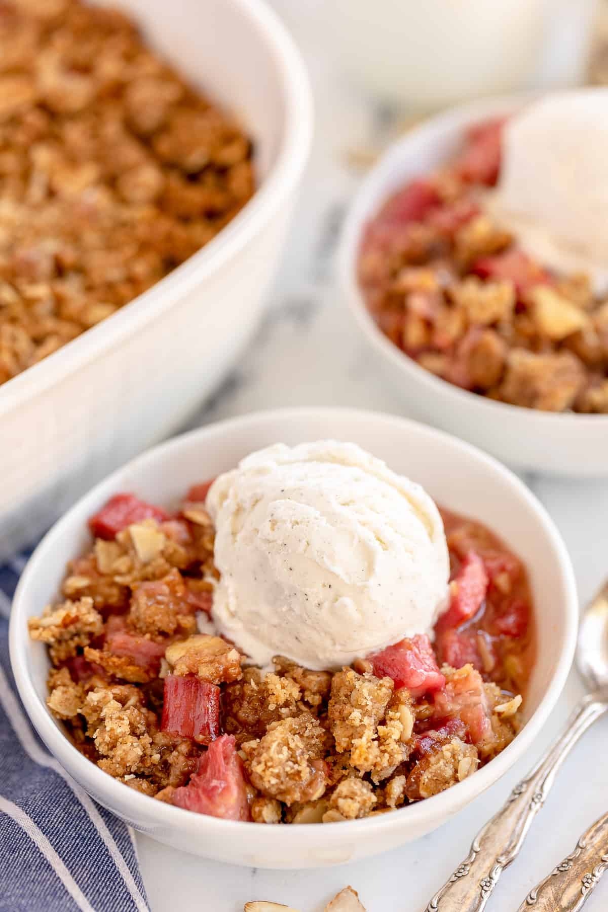 Rhubarb crisp in white bowls topped with vanilla ice cream.