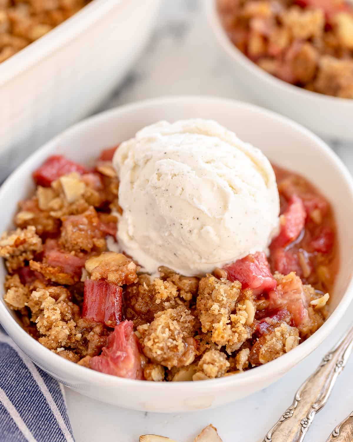 Rhubarb crumble in white bowls topped with vanilla ice cream.