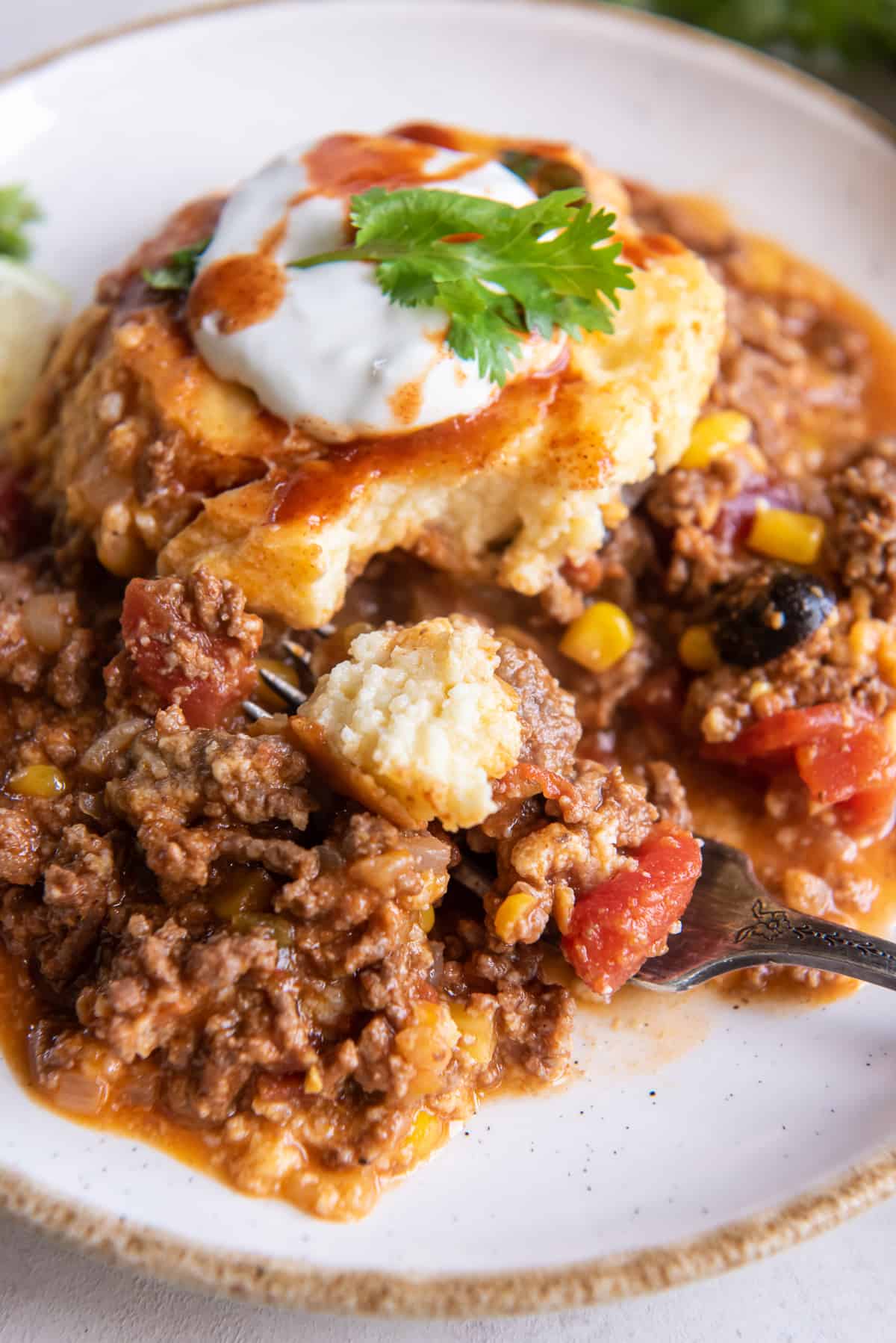 A fork digging into a serving of tamale pie on a white plate.