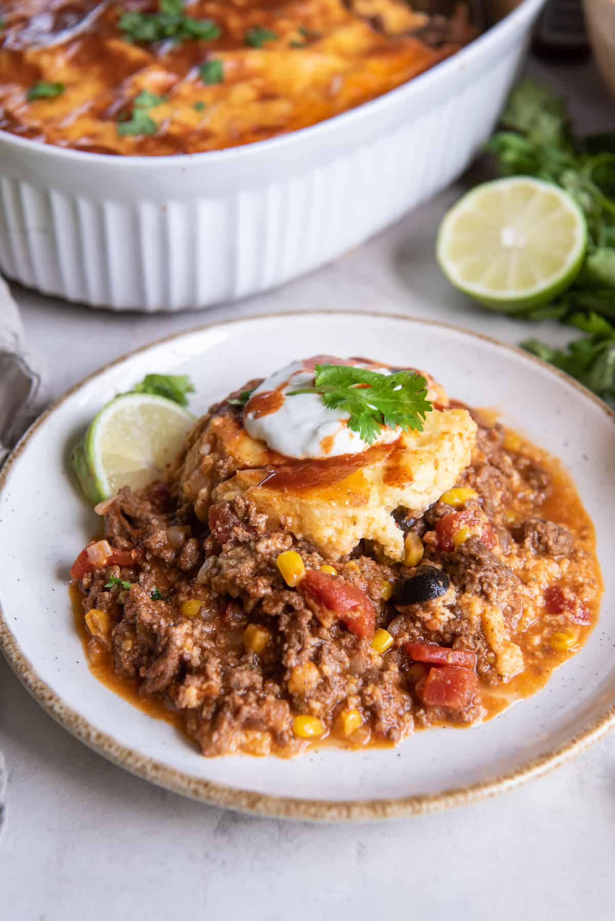 A serving of tamale pie topped with sour cream and hot sauce on a white plate.