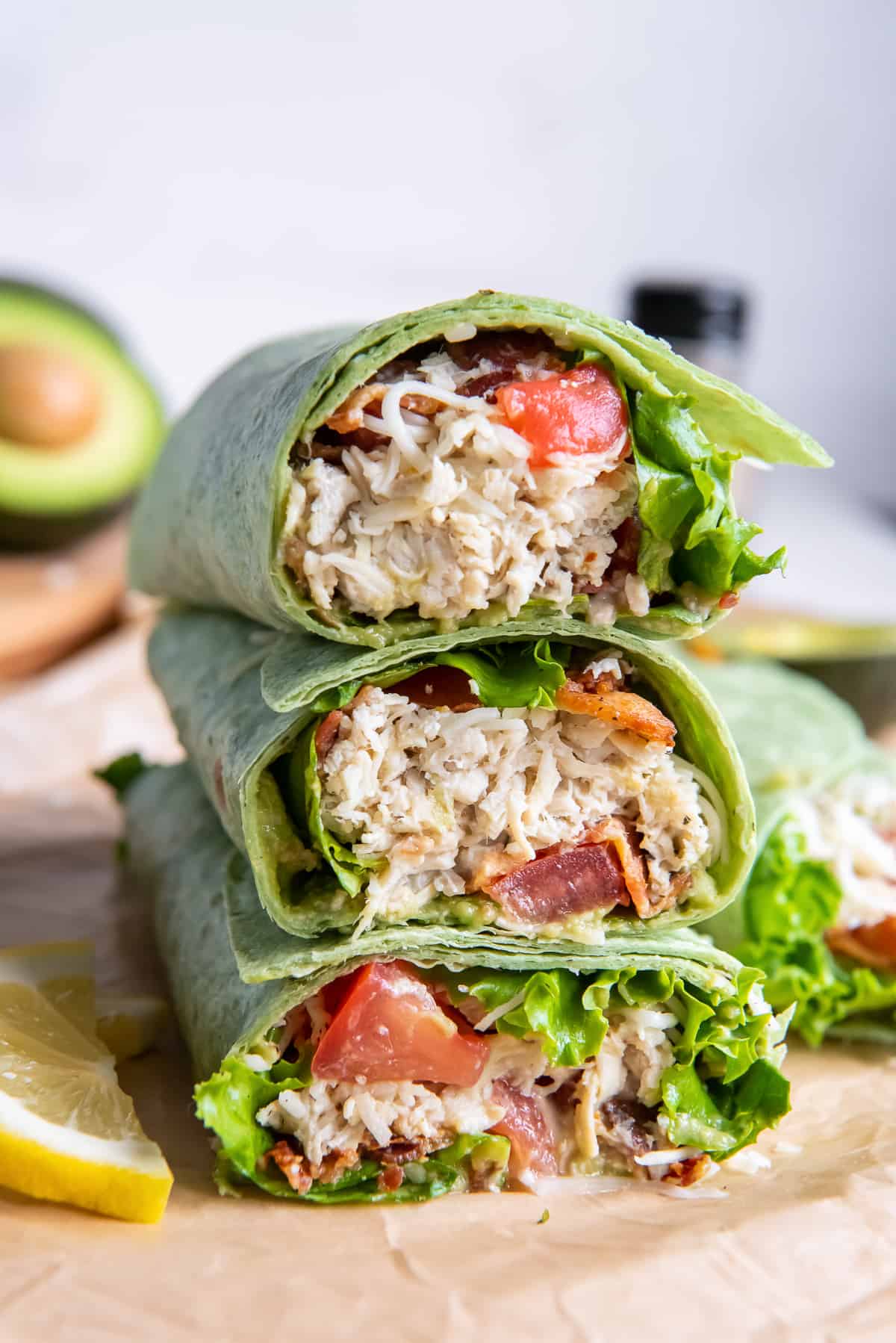 A California Club Chicken Wrap on a green spinach tortilla sliced in half and stacked on a cutting board.