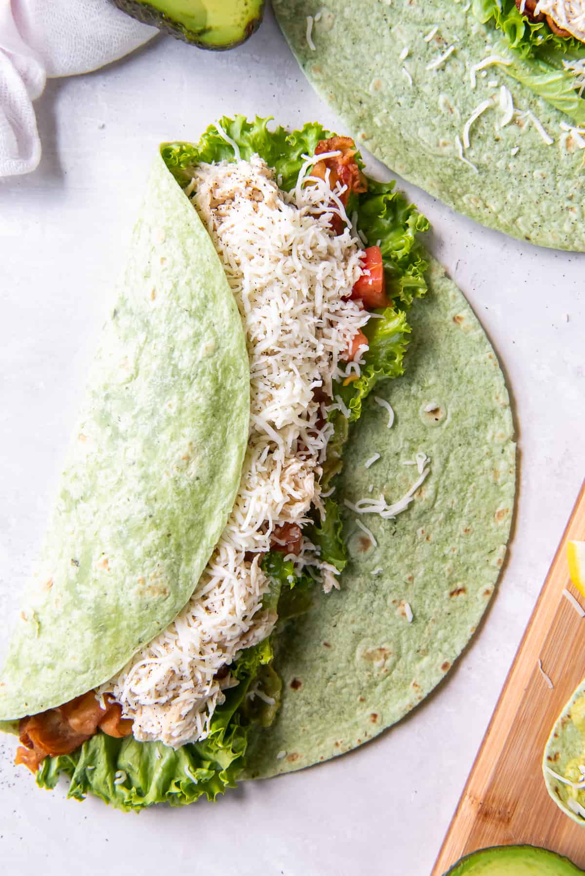 A green tortilla folded halfway over a chicken club mixture.