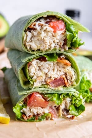 A chicken wrap on green tortilla sliced in half and stacked on a cutting board.