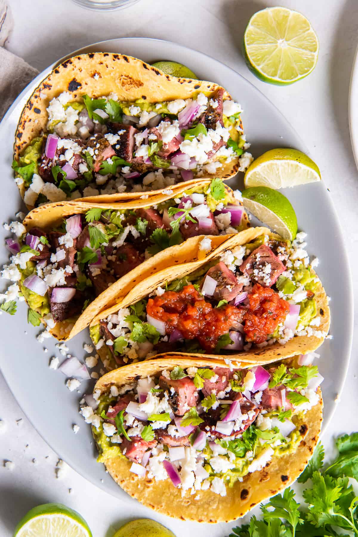 A top down shot of tacos with salsa, onions, and cotija cheese on a white platter.