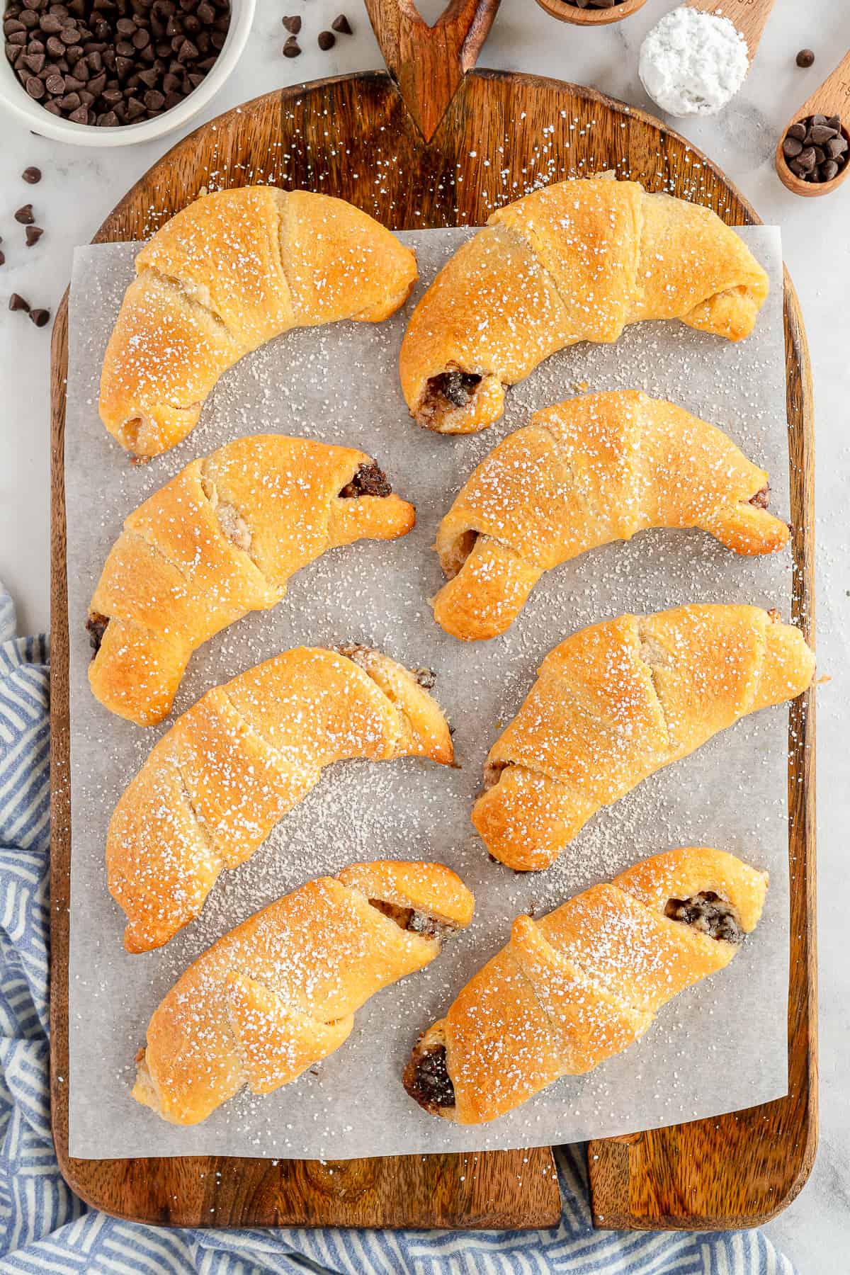 A top down shot of chocolate crescent rolls sprinkled with powdered sugar on a board.