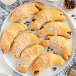 A top down shot of chocolate stuffed crescent rolls with powdered sugar on a white plate.