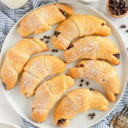 A top down shot of chocolate stuffed crescent rolls with powdered sugar on a white plate.