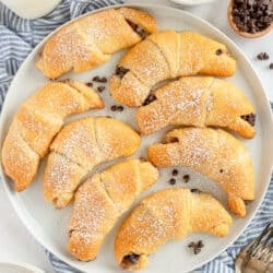 A top down shot of chocolate stuffed crescent rolls with powdered sugar on a white plate.