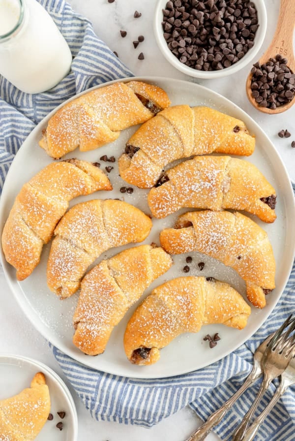 A top down shot of chocolate stuffed crescent rolls with powdered sugar on a white plate.