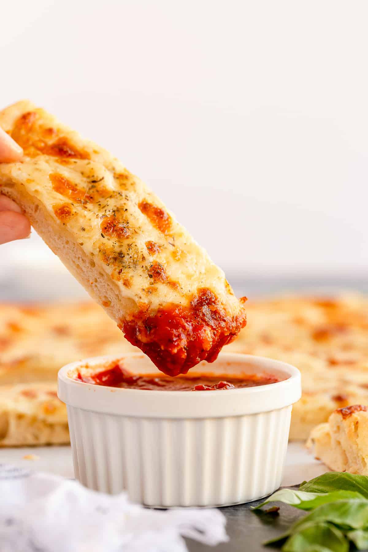 A cheesy breadstick dipping into marinara sauce from the side.