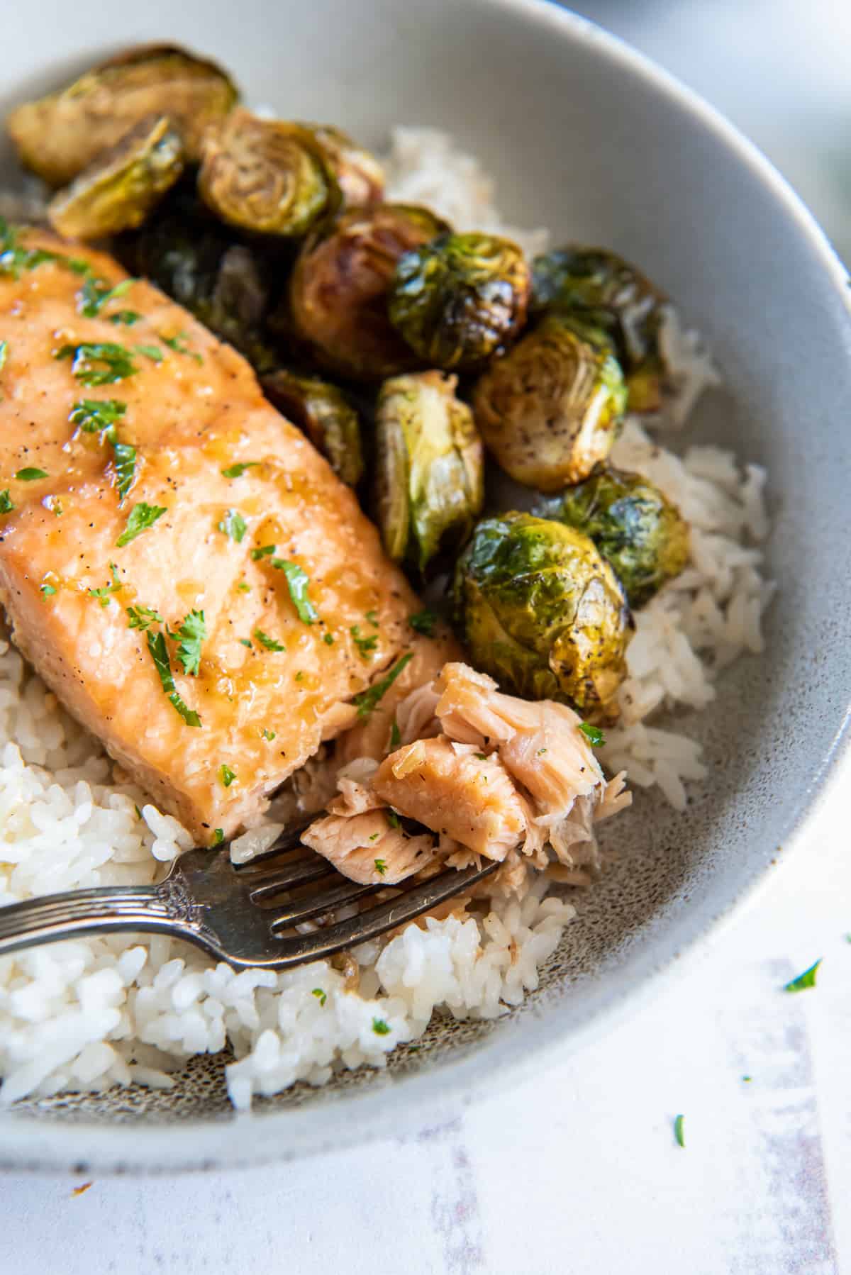 A fork breaking into salmon in a bowl with rice and brussels sprouts.