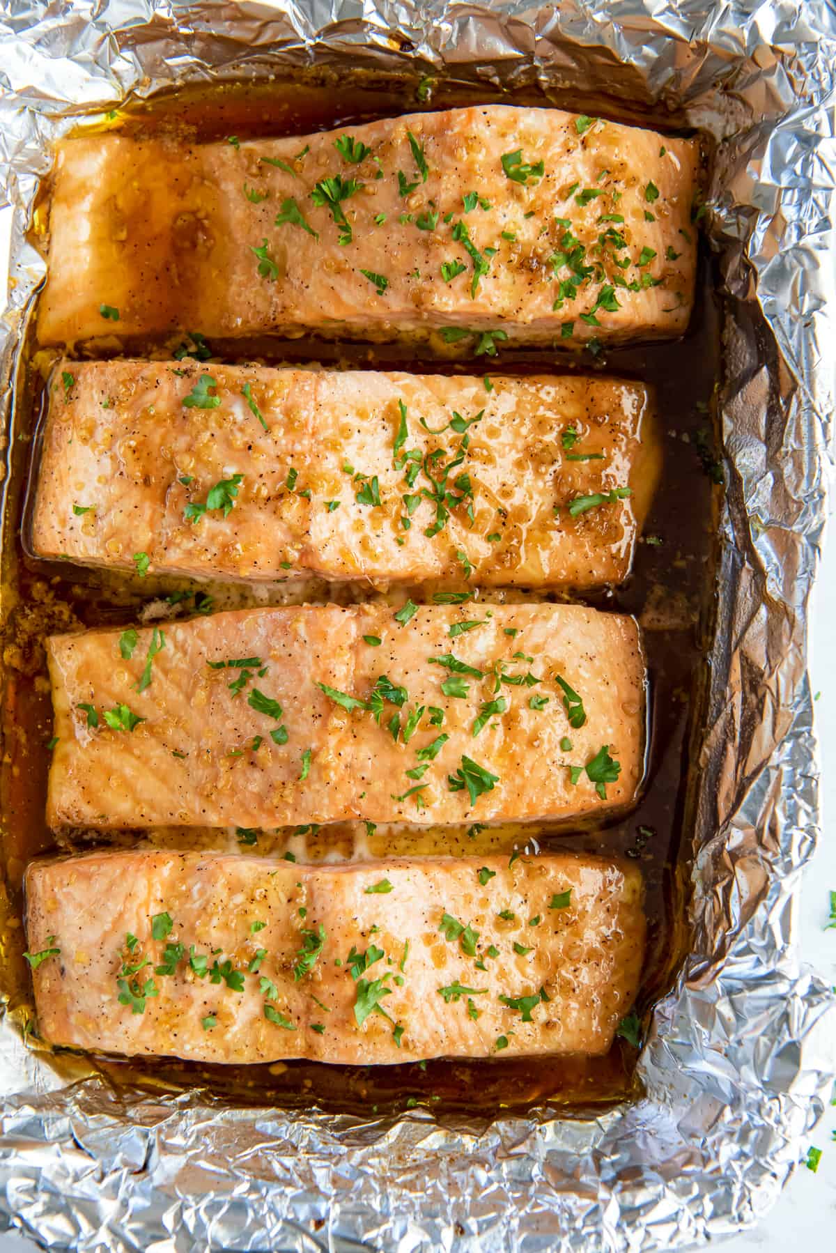 A top down shot of oven roasted salmon in a foil lined baking dish.
