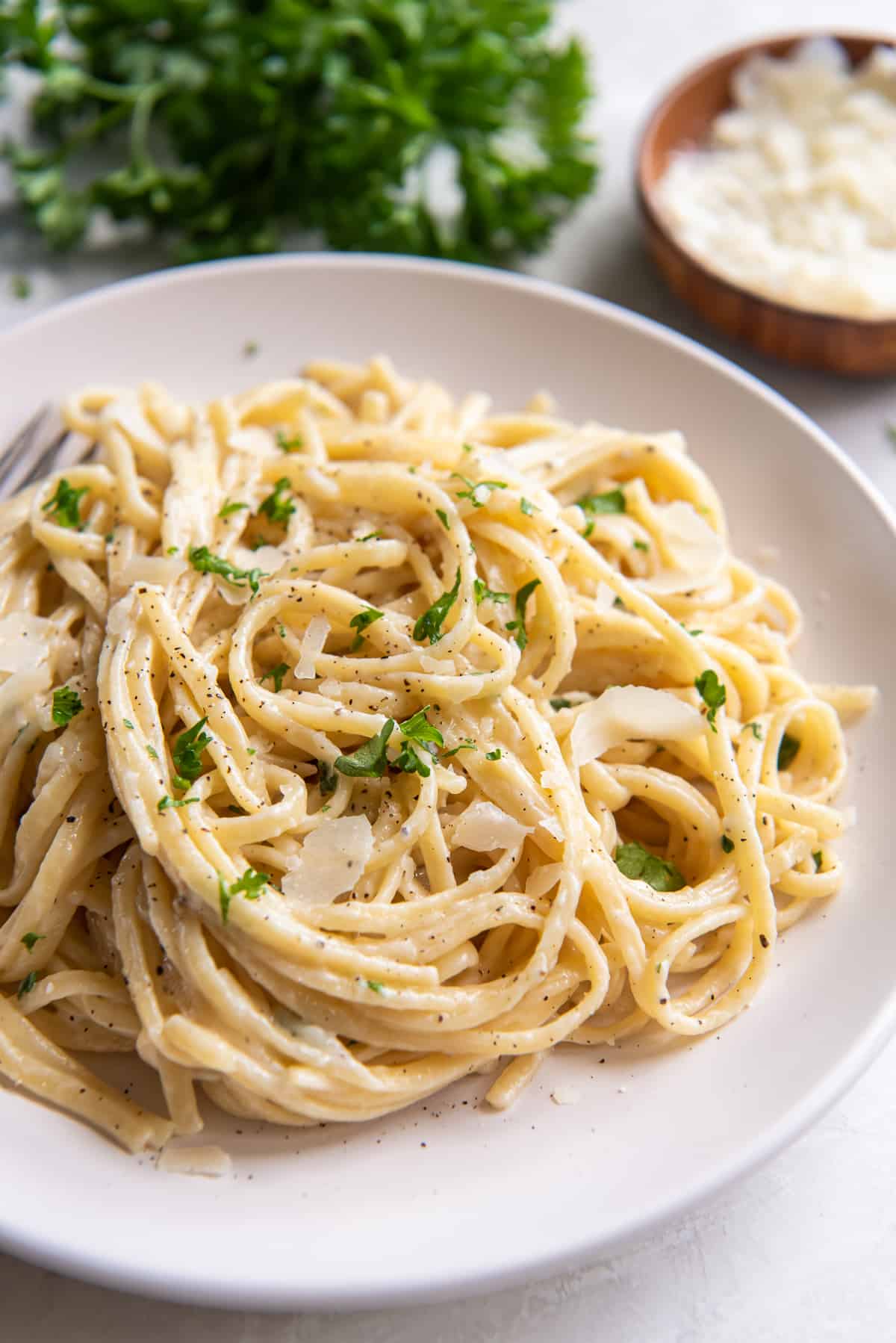 Parmesan noodles on a white plate with parsley and Parmesan in the background.