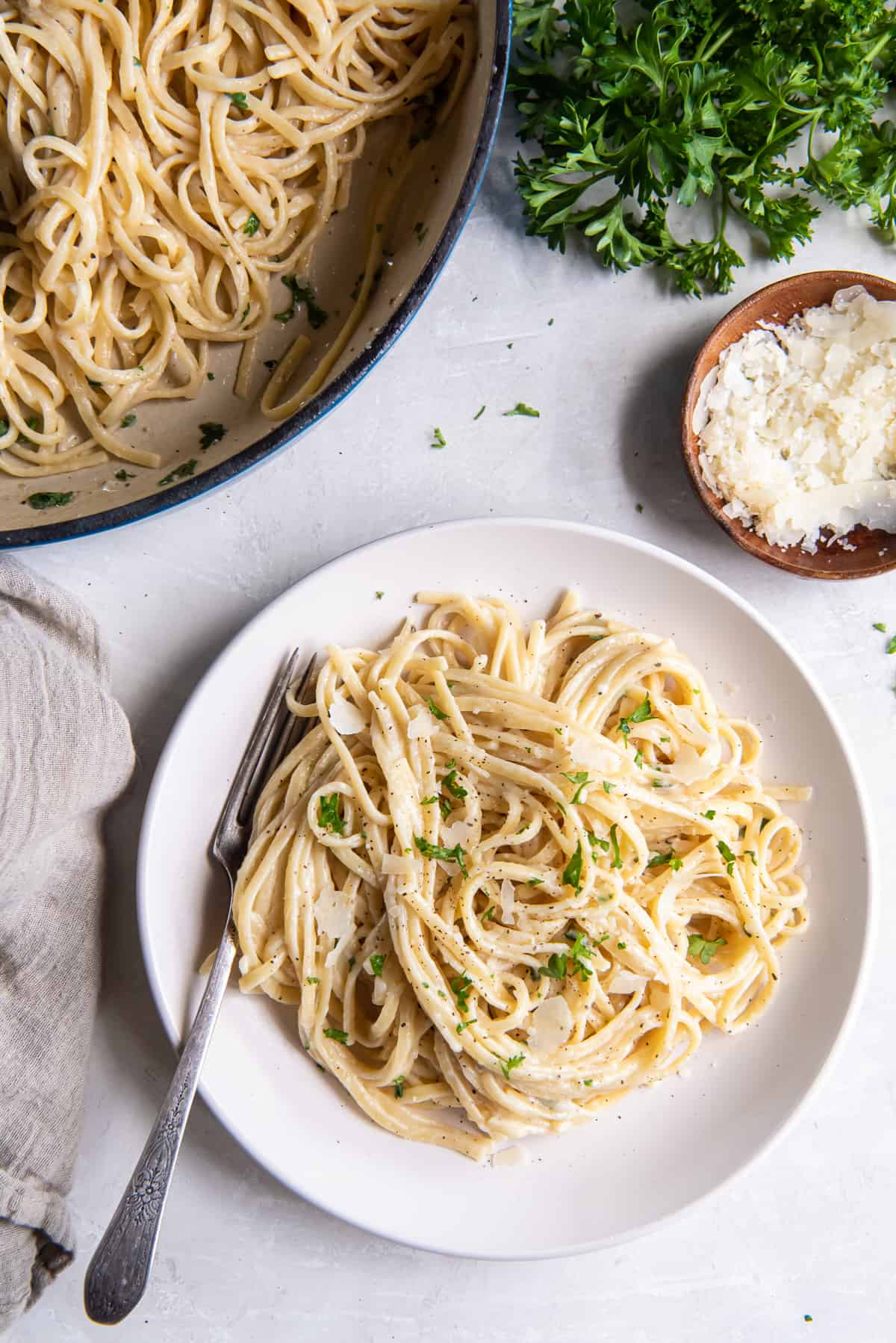 A top down shot of Parmesan Noodles in a skillet and on a white plate with a fork.