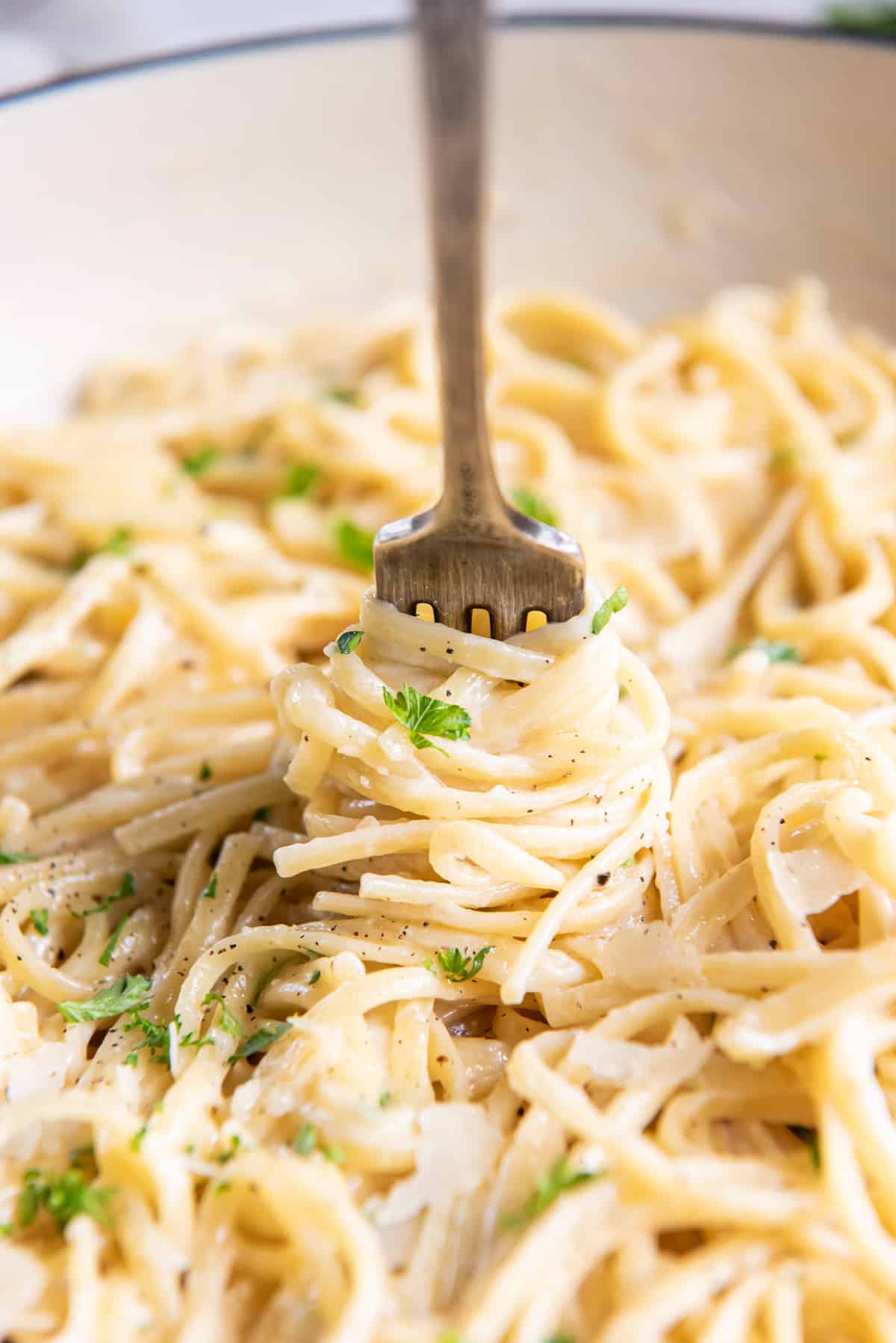 A fork twirls cooked linguine in a skillet.