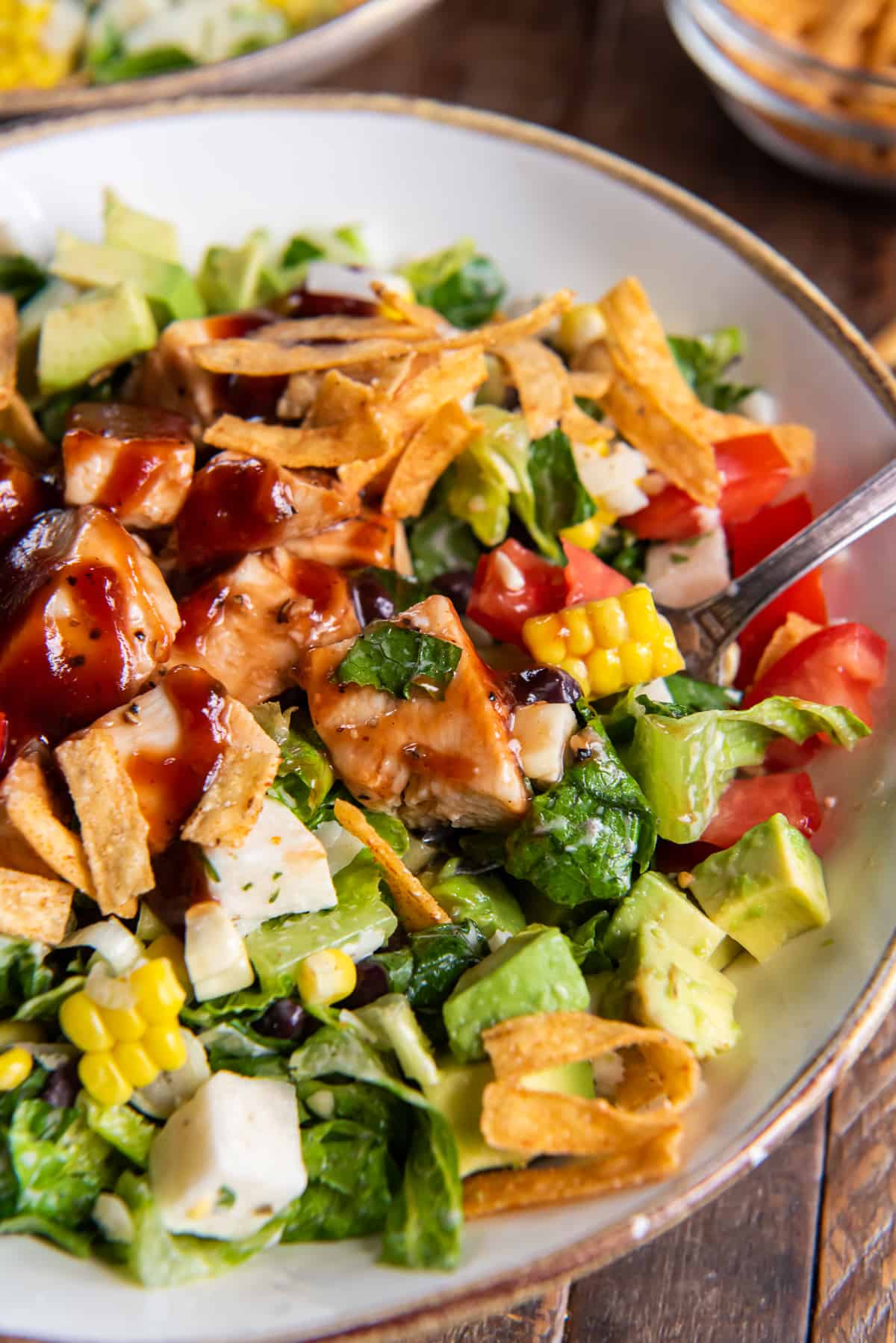 A chicken salad in a white bowl topped with bbq sauce and tortilla strips.