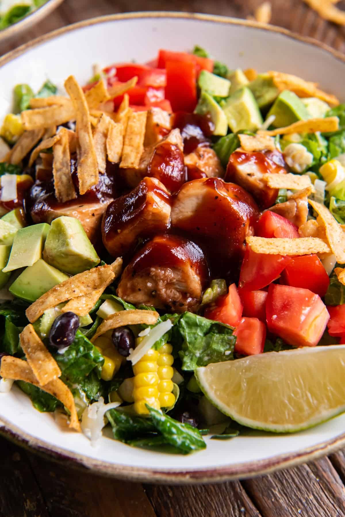 A close up of a chicken salad in a white bowl with a lime wedge.