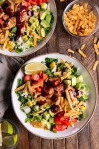 A top down shot of two salads with chicken, bbq sauce, tomatoes, and other ingredients.