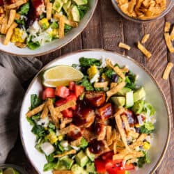 A top down shot of two salads with chicken, bbq sauce, tomatoes, and other ingredients.