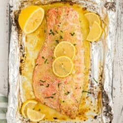 A top down shot of a large baked salmon fillet topped with butter and garlic sauce and lemon slices on a large sheet of foil.