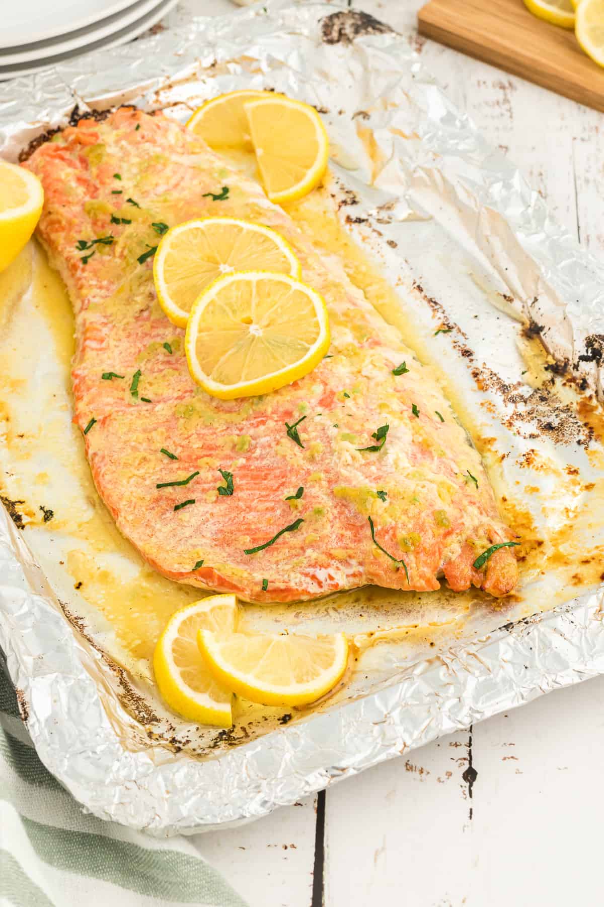 A large salmon fillet on foil topped with a garlic butter sauce and lemon slices.