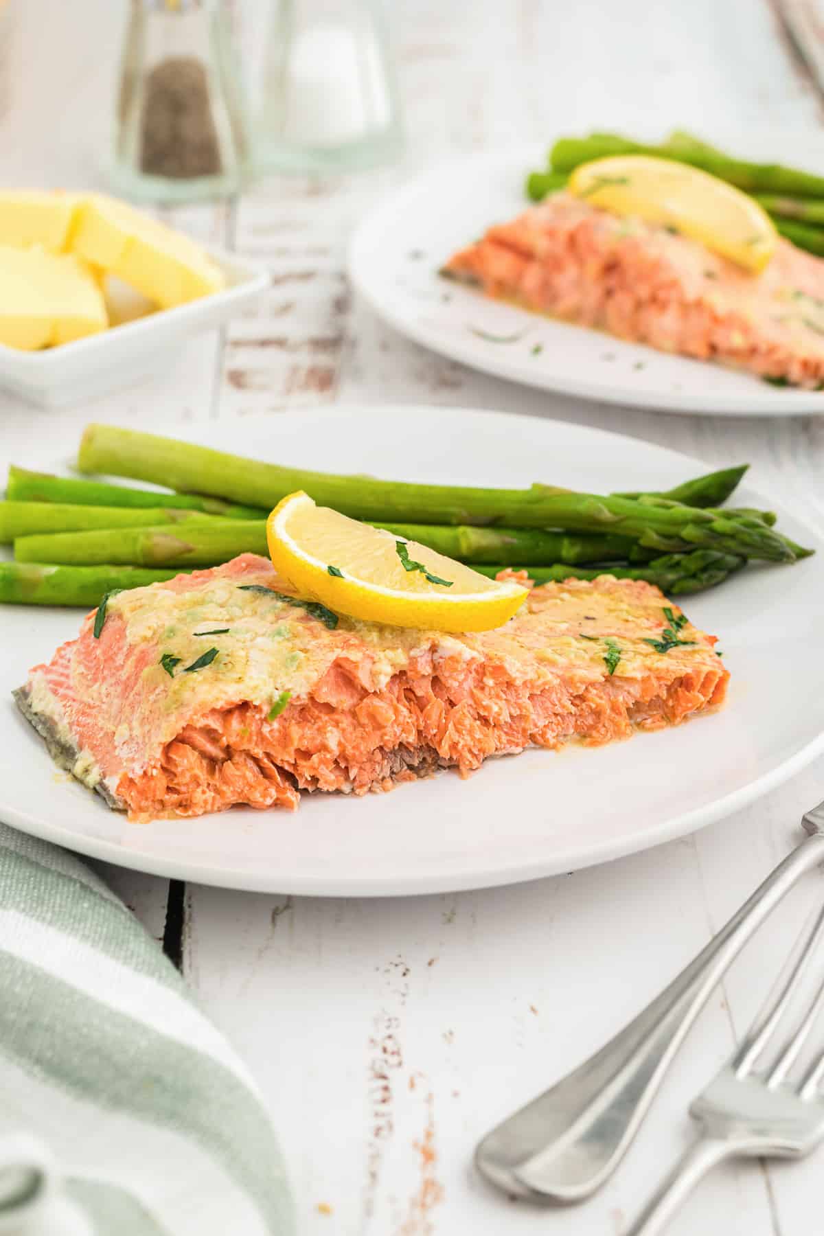 A slice of salmon topped with a slice of lemon on a white plate with asparagus.