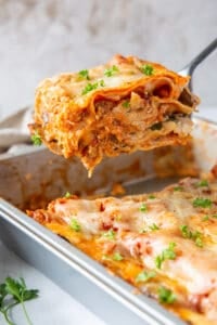 A spatula lifts a slice of lasagna from a metal baking dish.