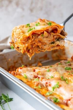 A spatula lifts a slice of lasagna from a metal baking dish.