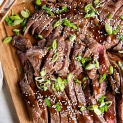 Sliced steak with teriyaki sauce topped with green onions on a wood cutting board.