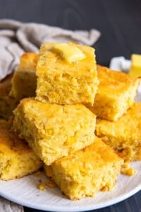 A piled of pieces of Mexican cornbread topped with a pat of butter on a white plate.