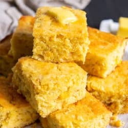 A piled of pieces of Mexican cornbread topped with a pat of butter on a white plate.