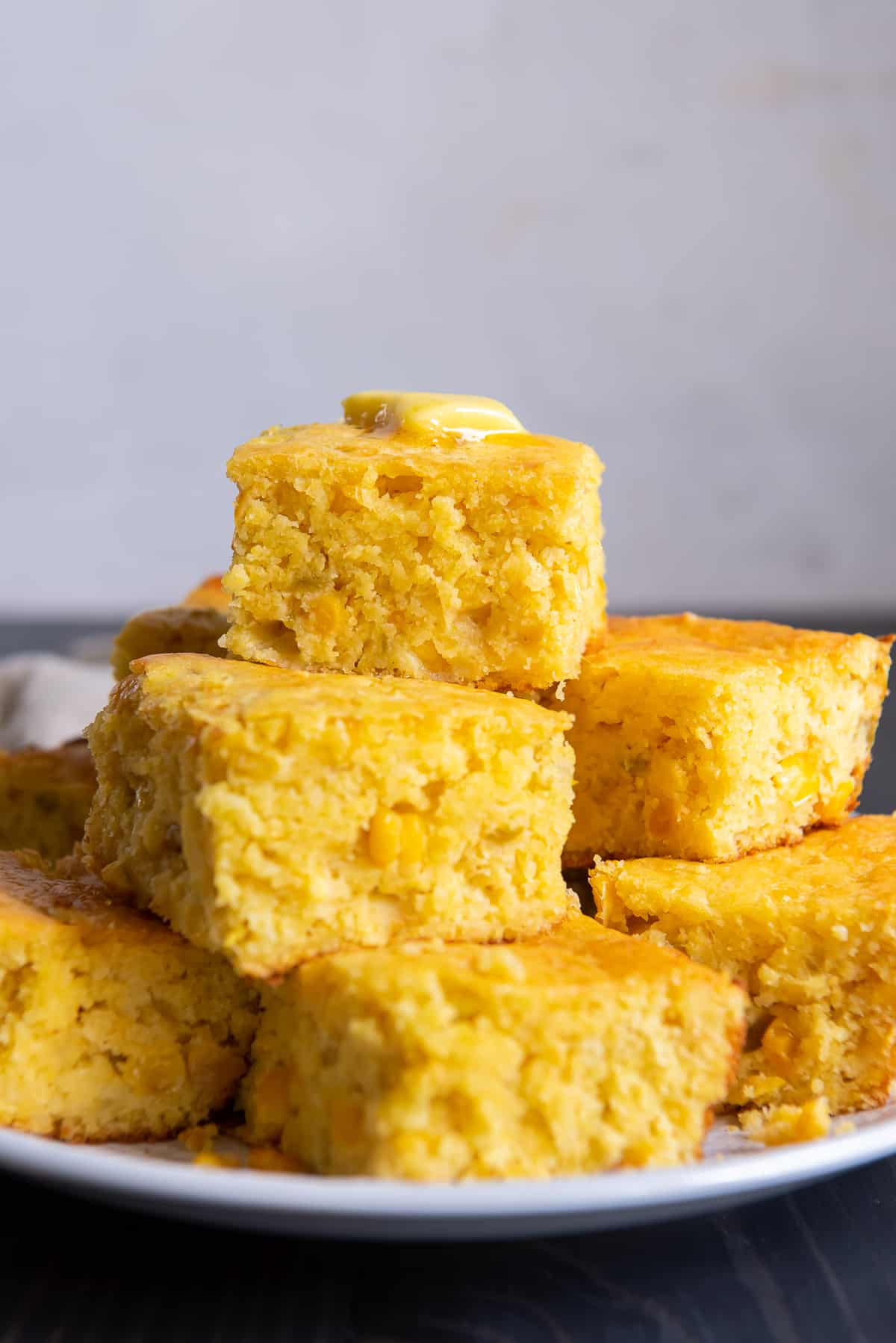 Slices of Mexican cornbread topped with butter on a white plate.