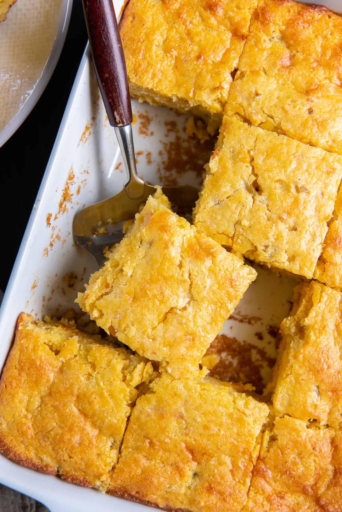 A top down shot of sliced cornbread in a white baking dish with a spatula.